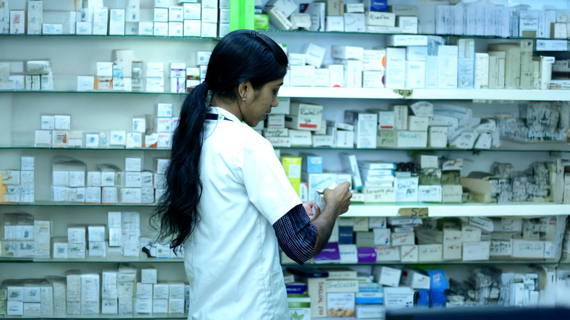 Trusted Indian pharmacist standing in a pharmacy with medicine shelves.